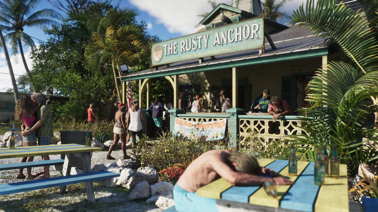 Bar de playa de madera con el rótulo The Rusty Anchor y una pancarta de festival del cangrejo. Hay gente en la terraza y un hombre dormido sobre una mesa de picnic.