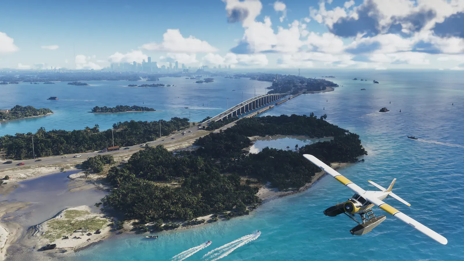 Vista aérea de islas bajas cubiertas de vegetación unidas por un puente largo sobre agua turquesa. Un hidroavión cruza en primer plano y al fondo se recorta una ciudad de rascacielos.