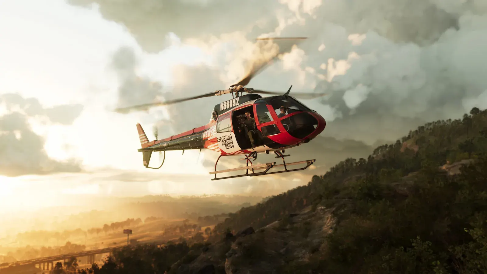 Helicóptero de una cadena de noticias volando sobre colinas boscosas al atardecer, con un cámara asomado por la puerta abierta.