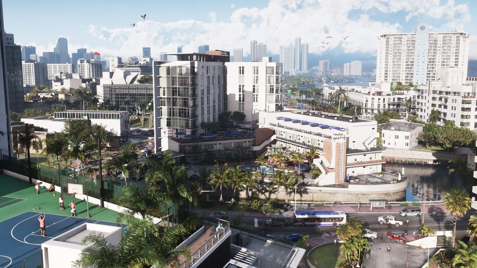 Vista elevada de Vice City: hoteles blancos de estilo art déco, una pista de baloncesto, palmeras, un autobús en la avenida y los rascacielos y la bahía al fondo.
